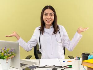 young-female-doctor-white-coat-with-stethoscope-around-her-neck-looking-front-smiling-spreading-arms-sides-sitting-table-with-laptop-light-wall_141793-52538.jpg