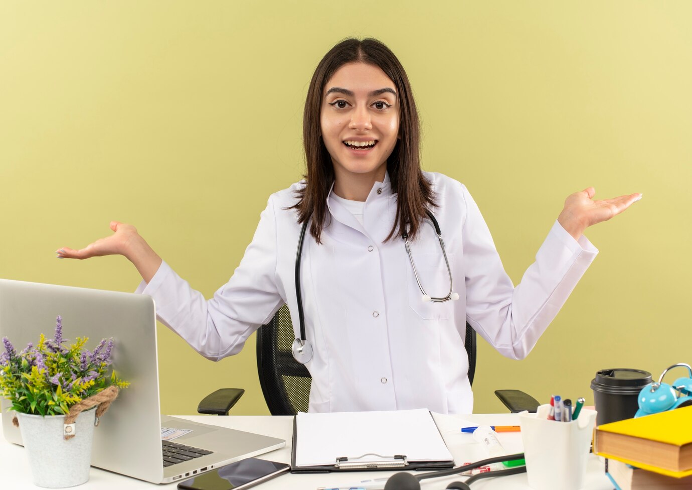 young-female-doctor-white-coat-with-stethoscope-around-her-neck-looking-front-smiling-spreading-arms-sides-sitting-table-with-laptop-light-wall_141793-52538.jpg